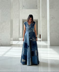 Woman wearing a long, patchwork denim dress in a marble hallway.