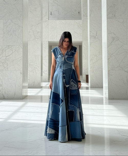 Woman wearing a long, patchwork denim dress in a marble hallway.